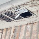 A broken air vent on the side of a building.