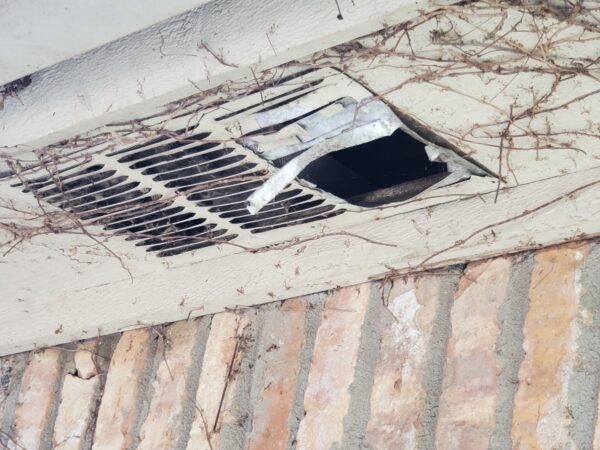 A broken air vent on the side of a building.