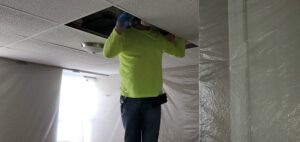 A man in yellow shirt inspecting an attic. Summertime Attic Work | Pest Control Services